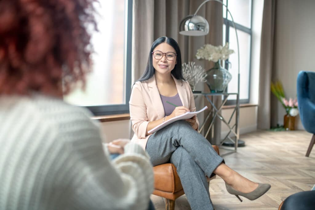 Why Choosing An EMDR Psychotherapist Can Accelerate Your Healing Professional woman with glasses taking notes during a counseling session in a bright office.